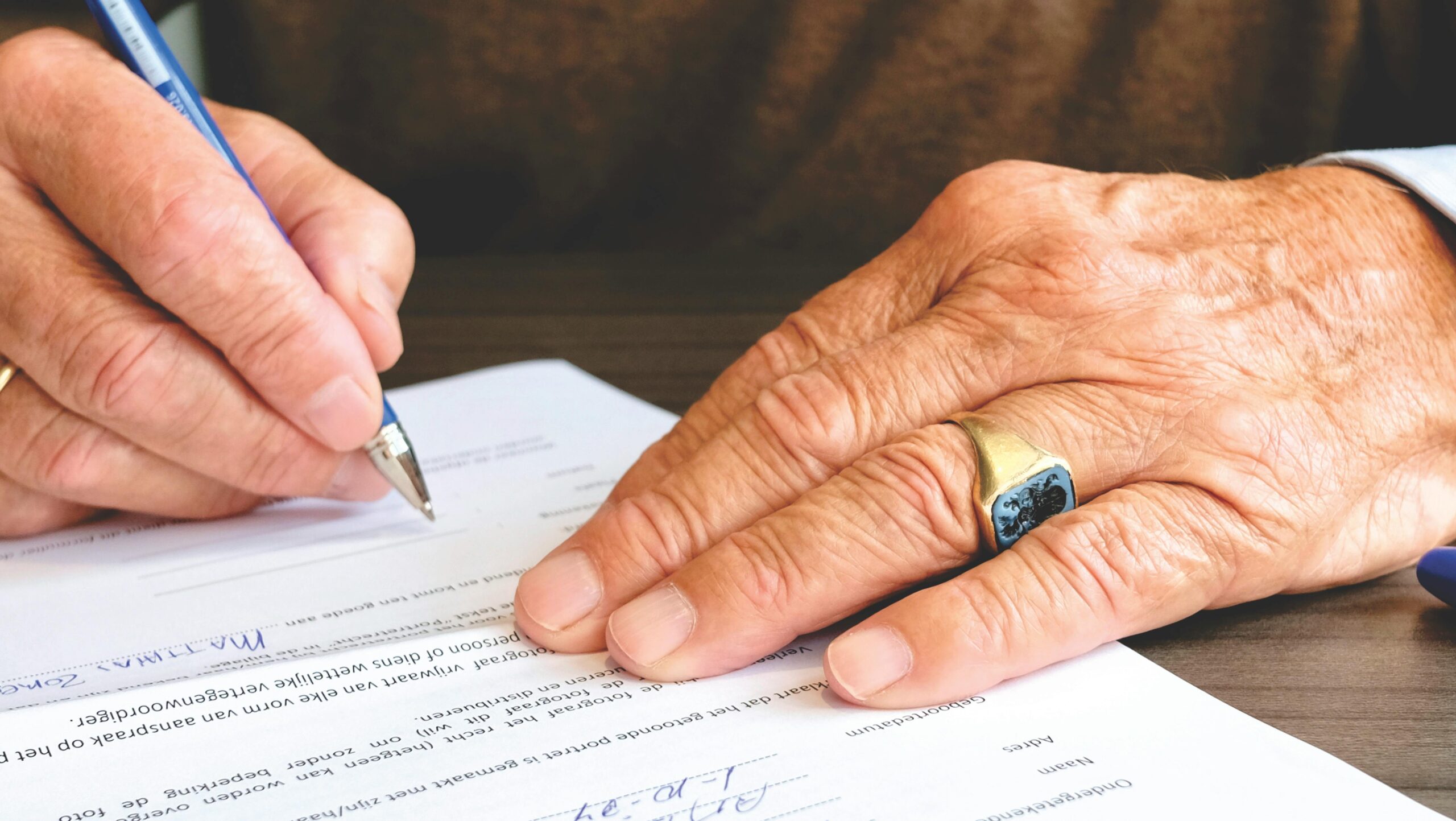 our-services-01 Close-up of a senior adult signing a legal document with a focus on hand and gold ring.